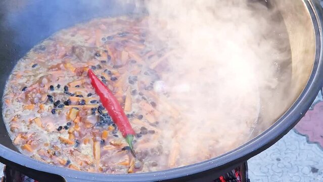 Cooking Uzbek pilaf. Boiling zirvak in a cast-iron cauldron on the grill