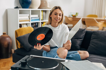 Pretty woman looking at the camera with vinyl record in her hand and gramophone in front of her.