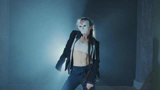 Fit girl in face mask dancing contemporary against blue smoke. Faceless young woman performing modern dance. Professional female dancer moves her body rhythmically at night party