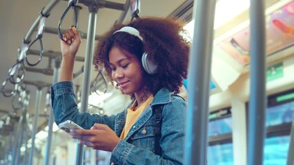Happy young African American woman passenger listening music via smart mobile phone in a train, Smile female wearing wireless headphones while moving in the tram, lifestyle, transportation. - Powered by Adobe