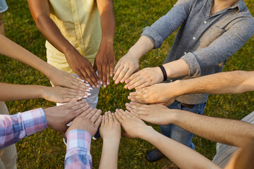 Diverse team of different young people standing in circle on green park lawn and joining their hands. Concept of teamwork, helping nature, and saving environment. Cropped shot, conceptual background