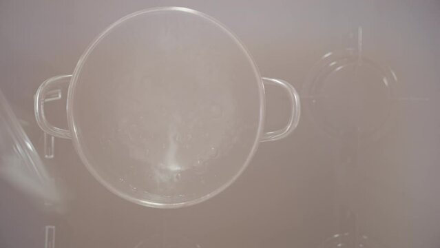 Using a red oven mitt to protect myself from burns, I lift the lid of the pot with boiling water. The view is from the top, and the scene is in slow motion.