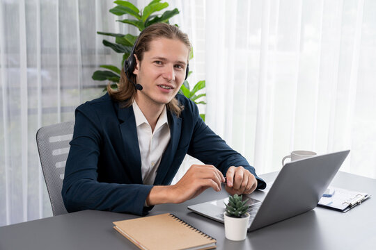 Male Customer Service Operator Or Telesales Agent Sitting At Desk In Office, Wearing Headset And Engage In Conversation With Client To Provide Support Or Close Sales. Call Center Portrait. Entity