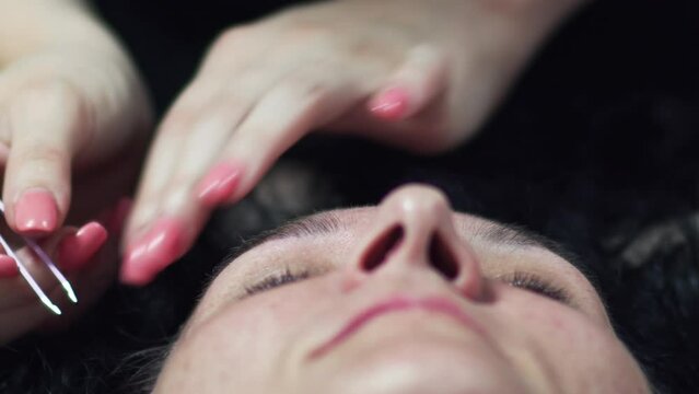 Closeup of beautician using tweezer for plucking and shaping the eyebrows of a woman in a beauty salon