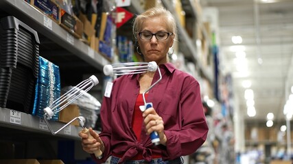 Attractive mature woman compares two paint rollers for best quality for home renovation project.