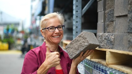 Attractive mature woman shopping looking at hardscaping bricks for home landscape improvement project.