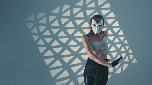 Flexible sexy girl with mask on face dances, squirming. Female dancer performs modern choreography for nightclub, party. Fit enigmatic woman moves rhythmically, shows hand waves