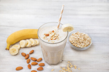 Banana smoothie with oat flakes and almond in glass. Healthy food. White wooden background. Copy space. 