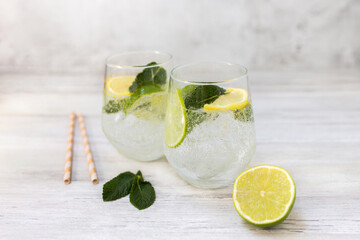 Cold refreshing lemonade drink or cocktail made of sparkling water, citrus and mint. Served drinking glass with ice cubes. On white wooden backgrond with copy space.  