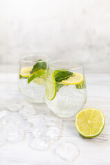 Cold refreshing lemonade drink or cocktail made of sparkling water, citrus and mint. Served drinking glass with ice cubes. On white wooden backgrond with copy space.  