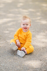 Funny kid toddler is sitting on the asphalt in a yellow suit