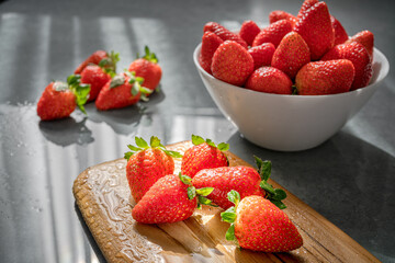 Strawberries arranged on a bowl and wooden tablets on a stone table and rays of sun.