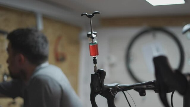 Bicycle mechanic holding syringe with brake fluid during brake bleeding process. Cycle repairman injects brake fluid into hydraulic brakes on bike in workshop. Maintenance cycle brake disc system. 