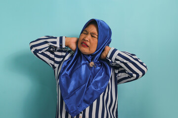 Asian woman in blue hijab massages neck/shoulders, relieving muscle pain from overwork, incorrect...