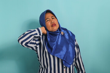 Asian woman in blue hijab massages neck/shoulders, relieving muscle pain from overwork, incorrect...