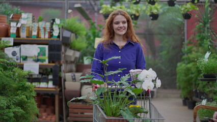 Happy Woman in walking through Horticulture Store aisle. Female Shopper with shopping Cart searching for Plant Purchases