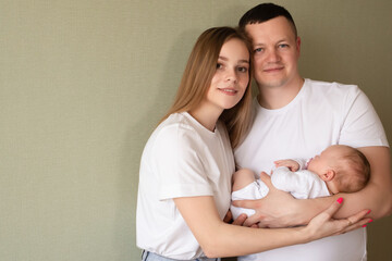  young parents hold the baby in their arms. dad and mom hug a small child. happy family relaxing at...