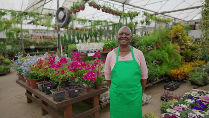 Fototapeta na wymiar An older florist female person. One Happy black senior woman wearing Apron standing inside Flower Shop portrait face close-up