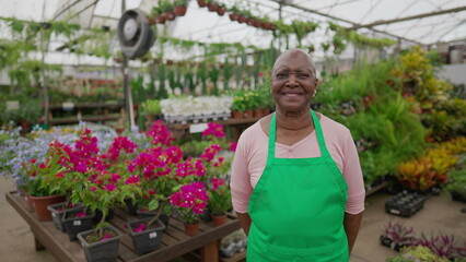 An older florist female person. One Happy black senior woman wearing Apron standing inside Flower Shop portrait face close-up