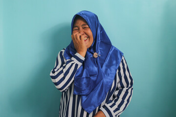 A funny Middle-Aged Asian woman, in a blue hijab and striped shirt, bursts into uncontrollable...