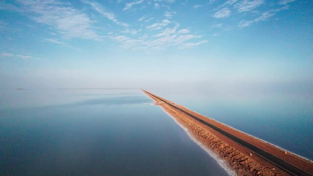 4K aerial view of beautiful road and salt water lake on both sides, connecting Khavda to Dholavira in Kutch, Gujarat, India. Road to heaven. Road trip. Clouds in sky with infinite road.