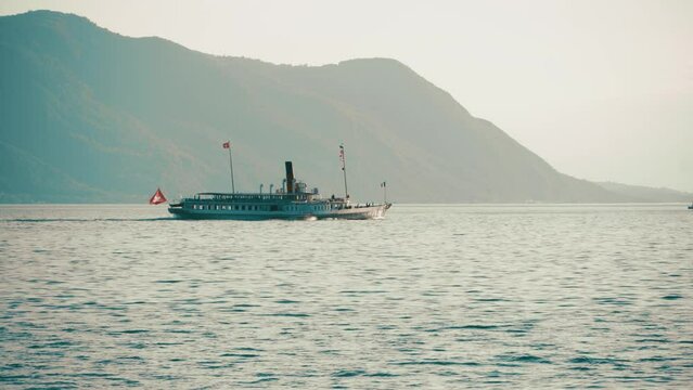 Lake Geneva in the evening against the backdrop of the Alpine mountains. Pleasure boat sails on Lake Geneva in the evening haze. Montreux, Switzerland