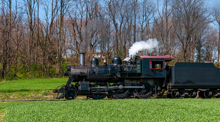 A Side View of a Restored Steam Locomotive Standing Still Blowing Smoke and Steam on a Sunny Day