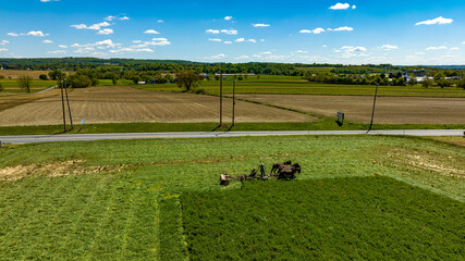 Obraz premium An Aerial View of an Amish Farmer Cutting Mowing Crops Using Four Horses and a Gas Engine and With the Countryside in View, on a Beautiful Summer Day