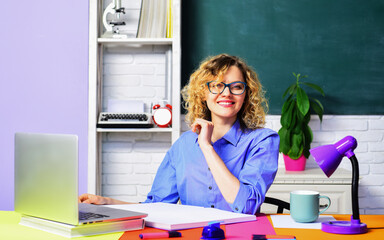 World teachers day. Professional teacher or university professor in classroom. Young teacher in glasses in school class. Student girl sitting at table with textbooks and laptop studying in auditorium.