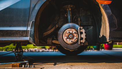 Wheel well of a vehicle lifted with a tire jack. Rusted hub and strut visible.