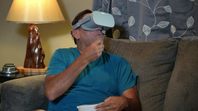A man watches a movie with his VR goggles while eating popcorn. Various reactions.  	