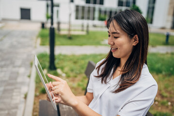 Young Japanese Business woman sitting in the street using a tablet and reading something

