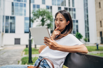 Fototapeta premium Young Japanese Business woman sitting in the street using a tablet and reading something
