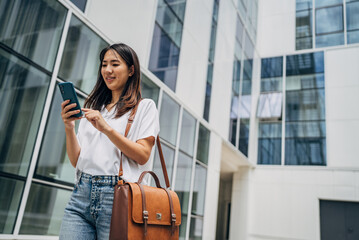 Young busy successful beautiful Japanese business woman, Japanese professional businesswoman holding cellphone using smartphone standing or walking on big city urban street outside