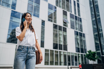 Young busy successful beautiful Japanese business woman, Japanese professional businesswoman holding cellphone using smartphone standing or walking on big city urban street outside
