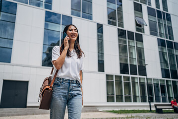 Young busy successful beautiful Japanese business woman, Japanese professional businesswoman holding cellphone using smartphone standing or walking on big city urban street outside