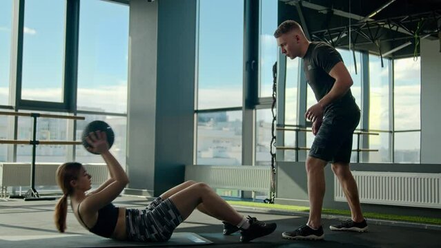 Sport woman girl training with male athlete doing sit ups on gym floor and throwing medicine ball to man sports trainer muscular couple bodybuilders sportsman and sportswoman workout in fitness club