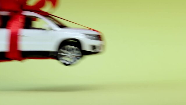 White model car with bow on a yellow background. Car as gift, surprise.