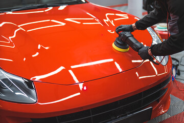 Car detailing concept. Worker with orbital polisher working on a red sports car in auto repair...