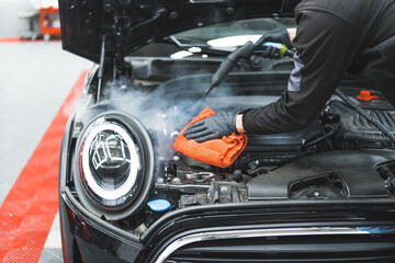 Car detailing concept. Manual engine cleaning with steam. Car detailing expert deep-cleaning black...