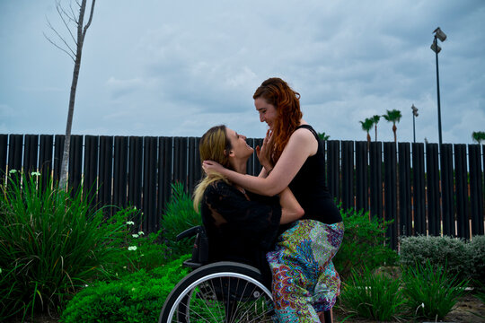 Loving woman sitting on knees of girlfriend with disability