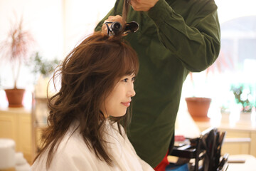 Naklejka premium 女性の髪にヘアアイロンをかける男性美容師