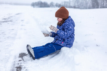 Fototapeta na wymiar Little girl in winter clothes sledding and having fun on the snow