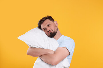 Unhappy man with pillow on yellow background. Insomnia problem