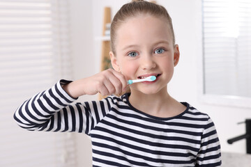 Cute little girl brushing her teeth with plastic toothbrush in bathroom