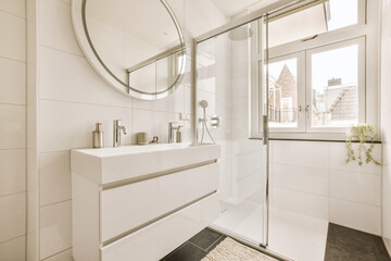 a modern bathroom with white tile walls and flooring, along with a large round mirror above the...