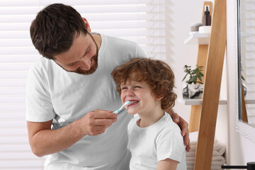 Fototapeta premium Father helping his son to brush teeth in bathroom