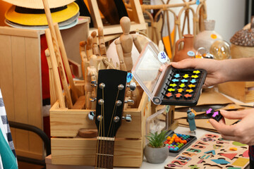 Woman holding smart game IQ near table with different stuff indoors, closeup. Garage sale