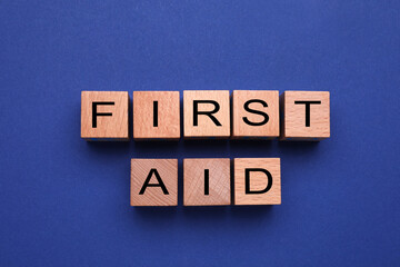 Words First Aid made of wooden cubes on blue background, flat lay