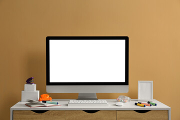 Stylish workplace with computer and stationery on wooden table near beige wall
